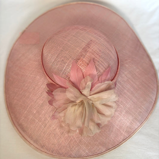 Pink wide-brim occasion hat with soft flower design and ribbon detail.