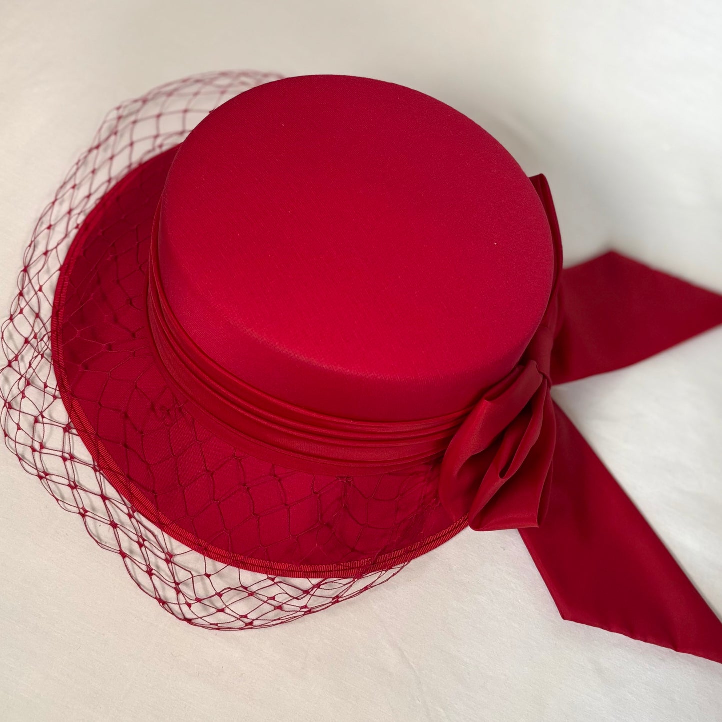 Red occasion hat with layered crown, soft bow and net detail