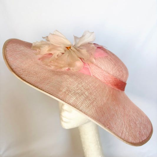 Pink wide-brim occasion hat with soft flower design and ribbon detail.
